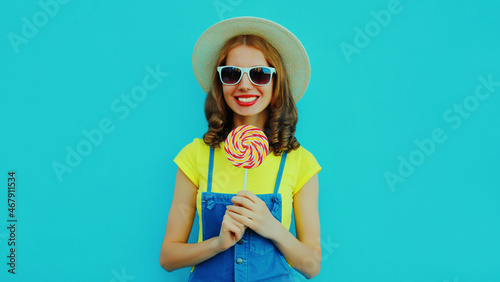 Summer portrait of happy smiling young woman with lollipop wearing a straw hat on blue background