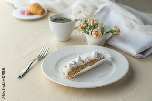 French desserts eclairs with white icing and cup of coffee on the table