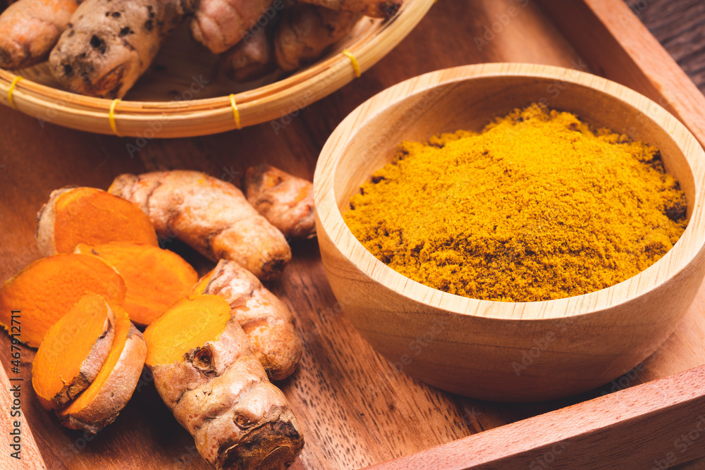Turmeric Powder and Turmeric root in wooden plate, Curry Powder on a wooden table background. Turmeric Powder and Turmeric root in wooden plate, Curry Powder on a wooden table background.