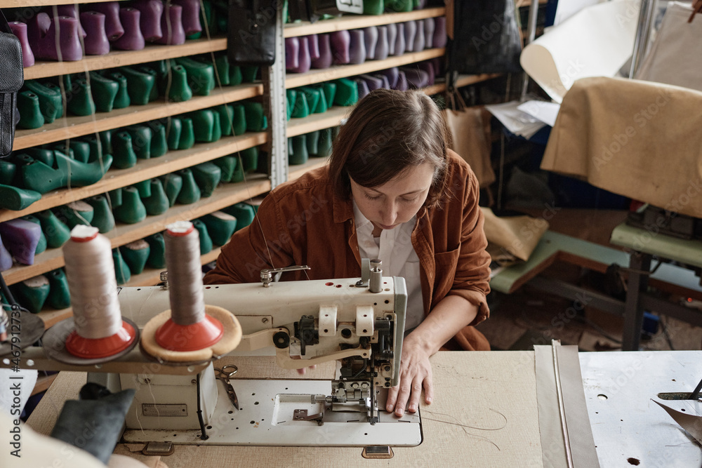 Shoemaker sitting at the table and using sewing machine in her work, she sewing new shoes Shoemaker sitting at the table and using sewing machine in her work, she sewing new shoes