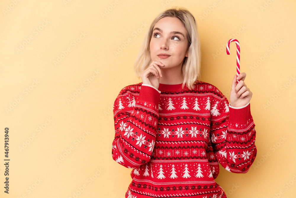Young caucasian woman holding a christmas stick isolated on yellow background looking sideways with doubtful and skeptical expression. Young caucasian woman holding a christmas stick isolated on yellow background looking sideways with doubtful and skeptical expression.
