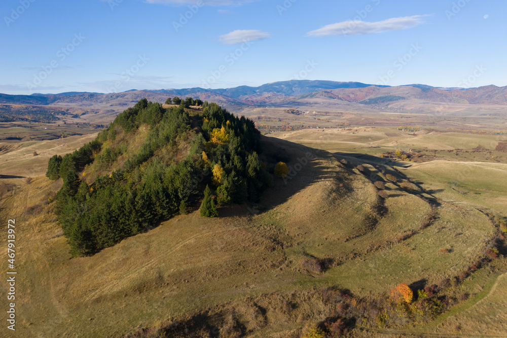 Aerial view of epic autumn landscape with evergreen covered hill and mountains.