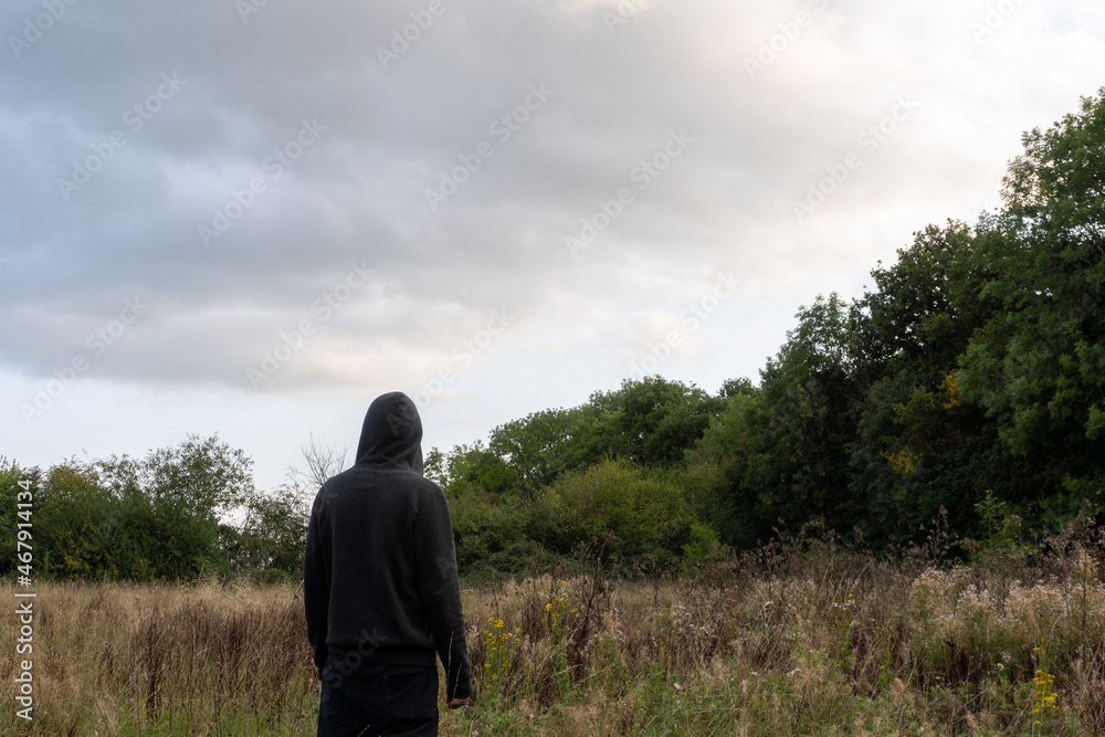 An atmospheric spooky edit of a hooded figure, back to camera. Standing in a field looking up at the sky. An atmospheric spooky edit of a hooded figure, back to camera. Standing in a field looking up at the sky.