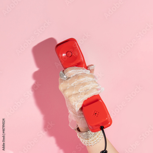 Creative layout with hand in white lace glove  holding red retro telepfone handset on pastel pink background. 80s or 90s retro aesthetic fashion concept. Romantic comunication idea. photo