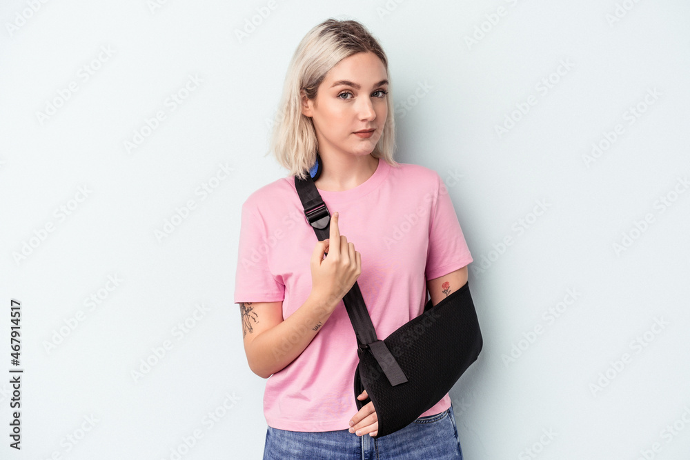 Young caucasian woman with broken hand isolated on blue background pointing with finger at you as if inviting come closer. Young caucasian woman with broken hand isolated on blue background pointing with finger at you as if inviting come closer.