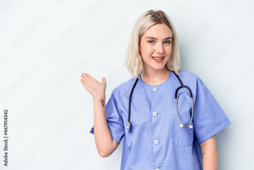 Young nurse woman isolated on blue background showing a copy space on a palm and holding another hand on waist. Young nurse woman isolated on blue background showing a copy space on a palm and holding another hand on waist.