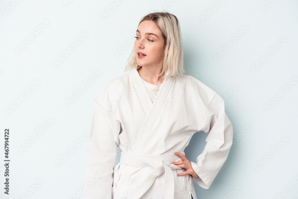 Young caucasian woman doing karate isolated on blue background looks aside smiling, cheerful and pleasant. Young caucasian woman doing karate isolated on blue background looks aside smiling, cheerful and pleasant.