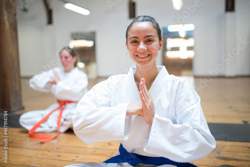 Happy young Caucasian girl smiling and sitting in karate pose. Cheerful female karatekas at karate academy. Sports, martial arts, healthy lifestyle concept