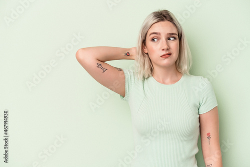 Young caucasian woman isolated on green background touching back of head, thinking and making a choice.