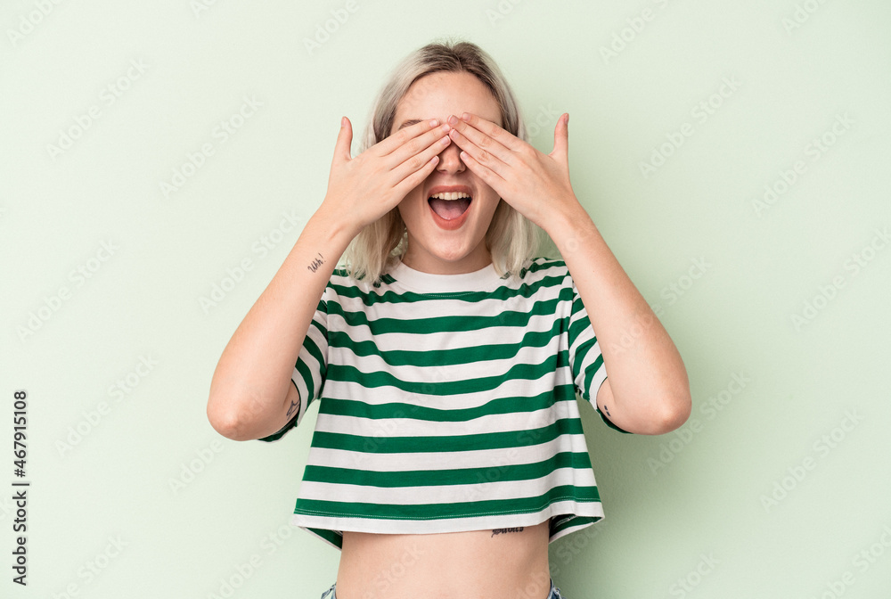 Young caucasian woman isolated on green background covers eyes with hands, smiles broadly waiting for a surprise. Young caucasian woman isolated on green background covers eyes with hands, smiles broadly waiting for a surprise.