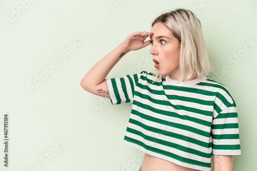 Young caucasian woman isolated on green background looking far away keeping hand on forehead. © Asier