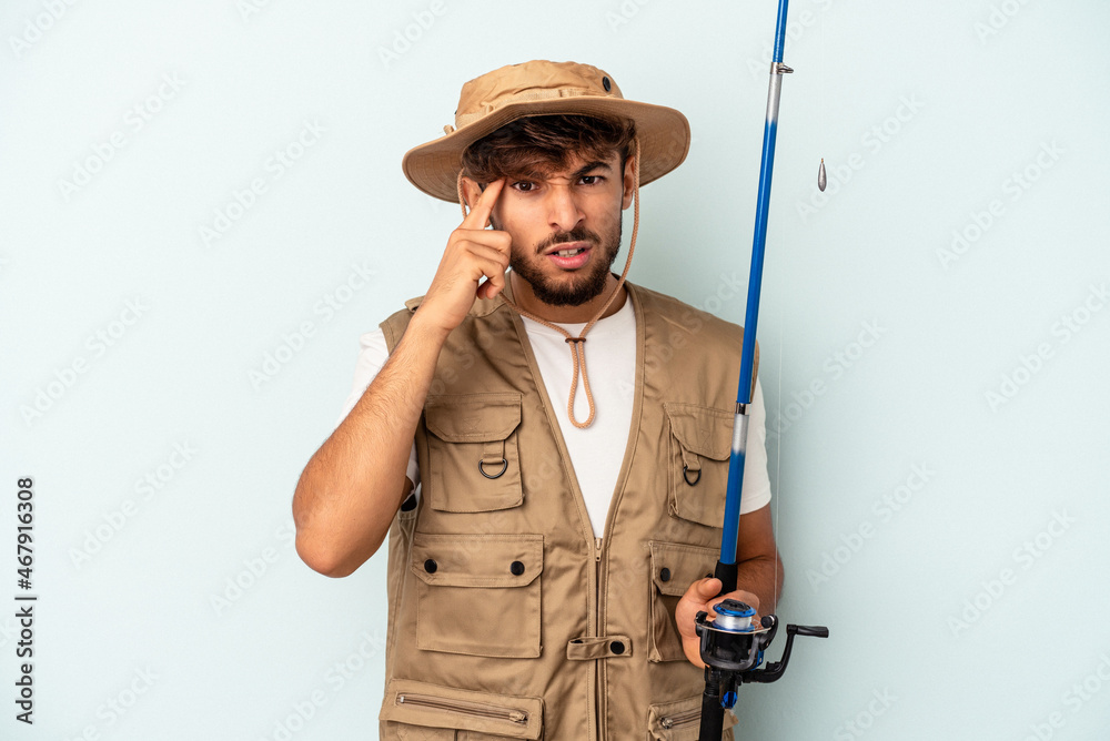 Young mixed race fisherman holding a rod isolated on blue background showing a disappointment gesture with forefinger. Young mixed race fisherman holding a rod isolated on blue background showing a disappointment gesture with forefinger.