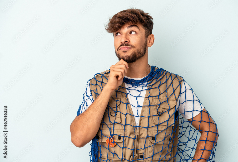 Young mixed race fisherman holding a net isolated on blue background looking sideways with doubtful and skeptical expression. Young mixed race fisherman holding a net isolated on blue background looking sideways with doubtful and skeptical expression.