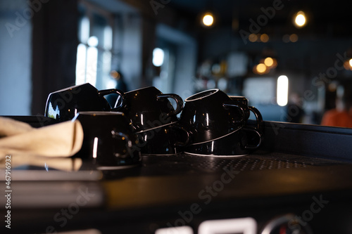 Pile of empty clean black coffee cups mugs on shelf or coffee machine in cafe indoors