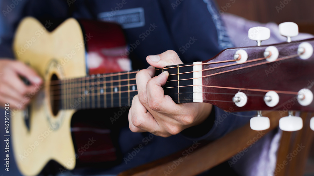Young man's hand practicing playing acoustic guitar, focus on hand.