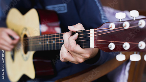 Young man's hand practicing playing acoustic guitar, focus on hand.