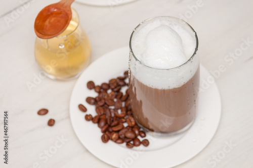 Glass coffee with foam milk with honey on white wooden table.