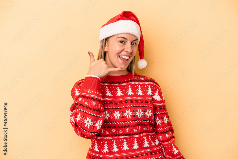 Young caucasian woman celebrating Christmas isolated on yellow background showing a mobile phone call gesture with fingers.