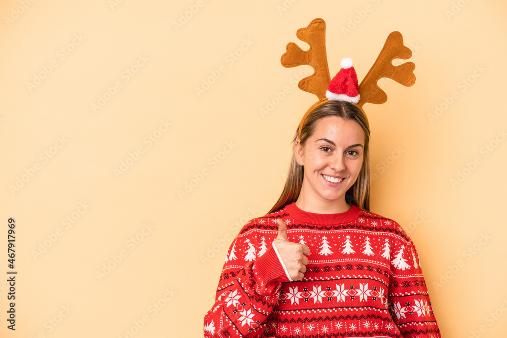 Young caucasian woman wearing a christmas reindeer hat isolated on yellow background smiling and raising thumb up Young caucasian woman wearing a christmas reindeer hat isolated on yellow background smiling and raising thumb up