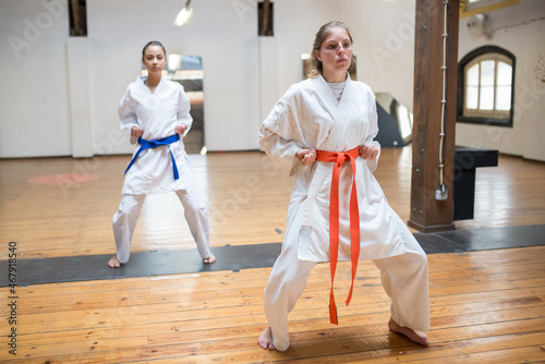 Focused young women at karate training. Attractive women in white clothes with blue and red belts warming up before training. Sport, healthy lifestyle concept