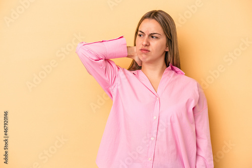 Young caucasian woman isolated on yellow background touching back of head, thinking and making a choice. © Asier