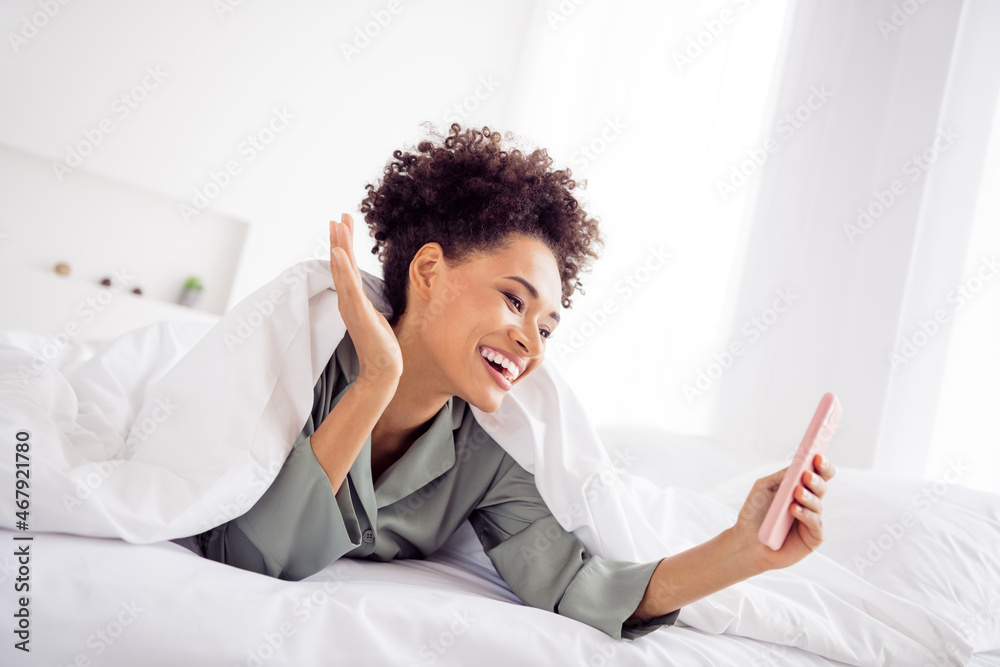 Portrait of attractive cheerful wavy-haired girl lying in bed using gadget calling video waving hello at light home house indoors Portrait of attractive cheerful wavy-haired girl lying in bed using gadget calling video waving hello at light home house indoors