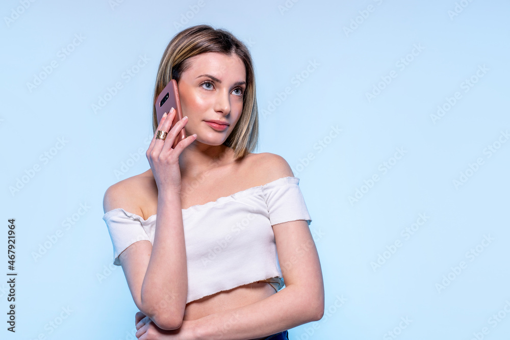Fototapeta premium Photo of young caucasian girl with light blue eyes using her cellphone with serious face for a call - Studio photography of pretty woman holding her telephone calling people