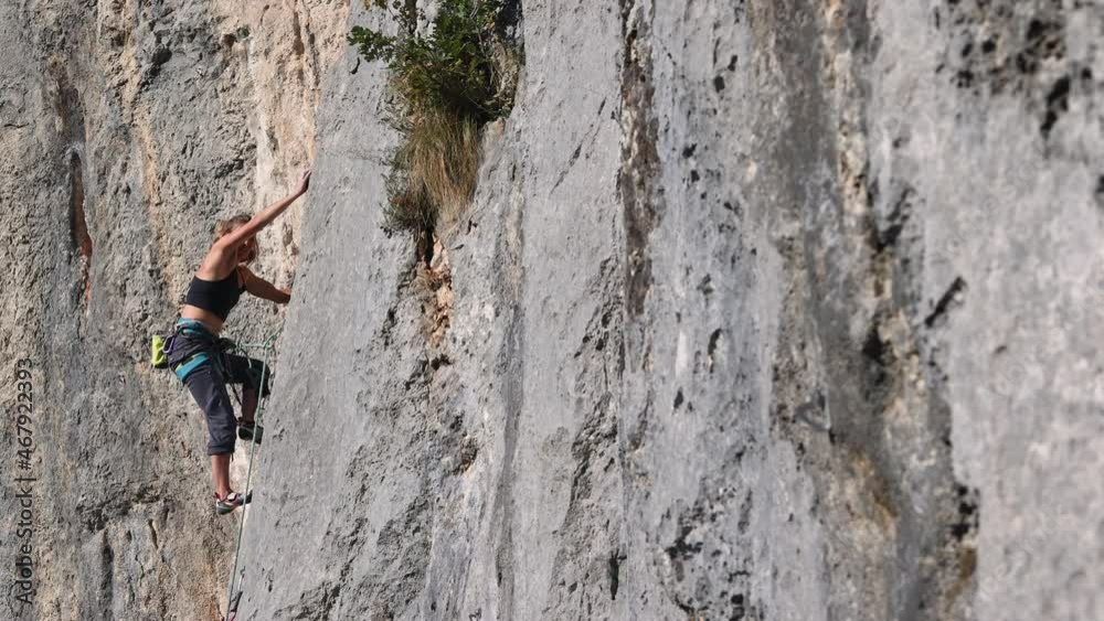 girl rock-climber climbs the rock against the background of the autumn forest and blue sky. a climber walks a difficult route using equipment.