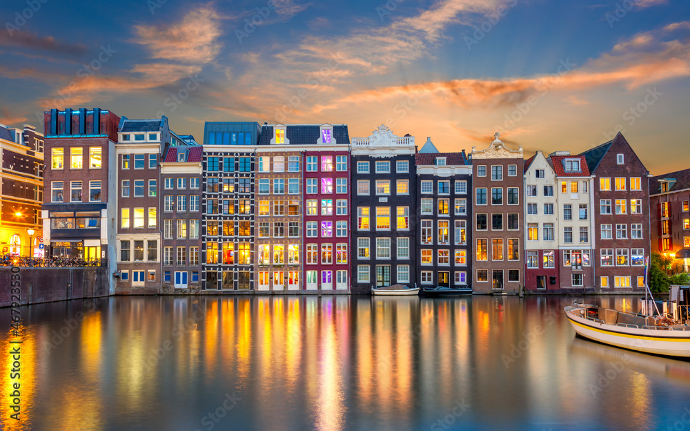 Old houses of Amsterdam in the evening. The houses stand in the water and have a beautiful reflection at night. Touristic district Damrak. These houses are famous all over the world. Amsterdam
