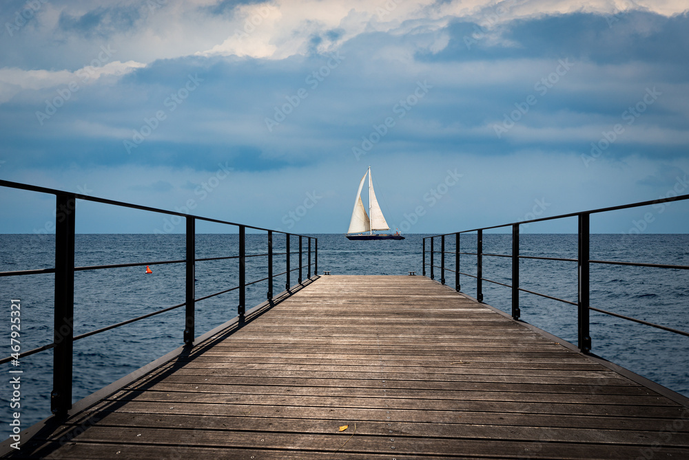 Naklejka premium Small empty wooden pier and a sailing boat in the horizon of the Mediterranean sea, Italy, Europe.
