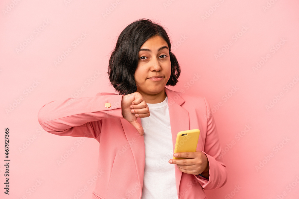 Young latin woman holding mobile phone isolated on pink background showing a dislike gesture, thumbs down. Disagreement concept. Young latin woman holding mobile phone isolated on pink background showing a dislike gesture, thumbs down. Disagreement concept.