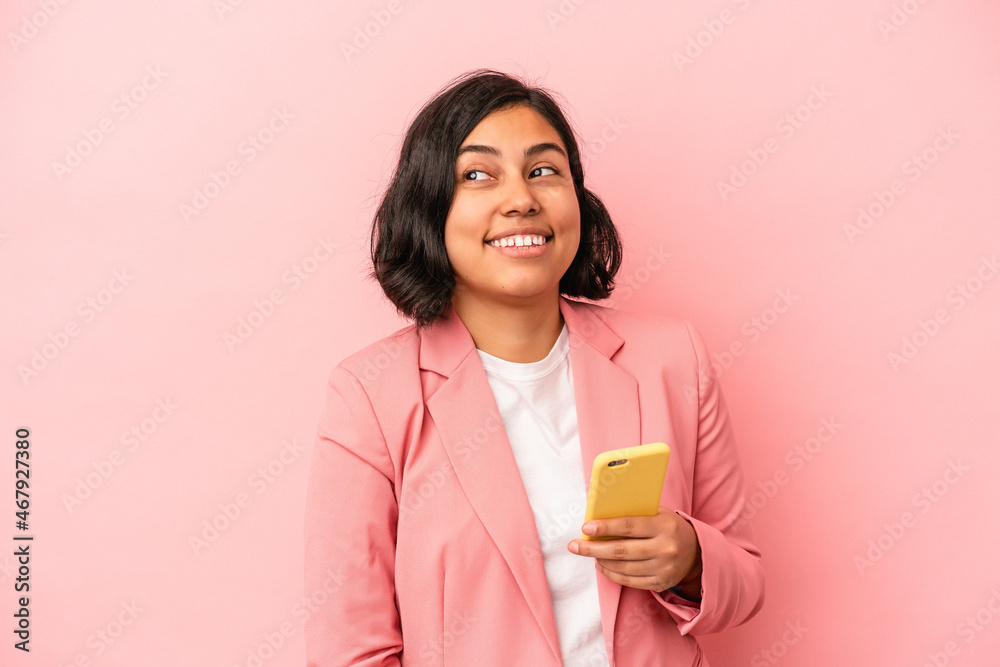 Young latin woman holding mobile phone isolated on pink background looks aside smiling, cheerful and pleasant. Young latin woman holding mobile phone isolated on pink background looks aside smiling, cheerful and pleasant.