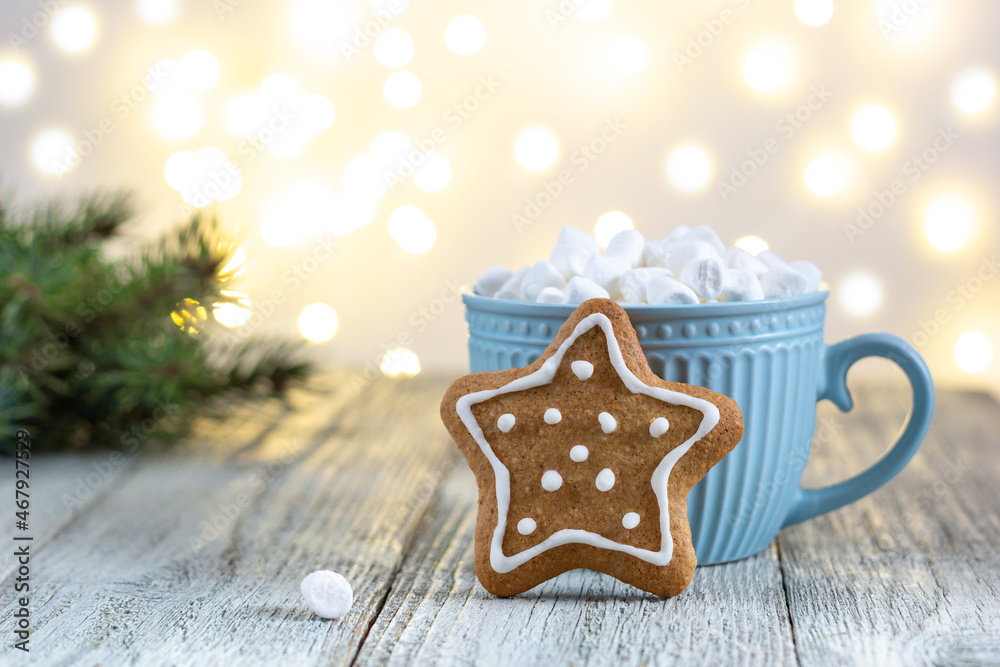 A blue cup of winter hot drink with marshmallows and gingerbread star on a white wooden background with bokeh. A blue cup of winter hot drink with marshmallows and gingerbread star on a white wooden background with bokeh.