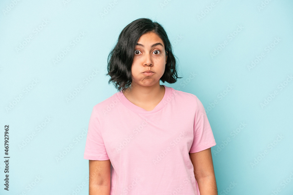 Young latin woman isolated on blue background blows cheeks, has tired expression. Facial expression concept. Young latin woman isolated on blue background blows cheeks, has tired expression. Facial expression concept.