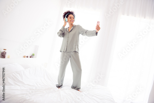 Photo of positive blogger lady stay bed make morning phone vlog wear earphones silky gown in light bedroom home indoors
