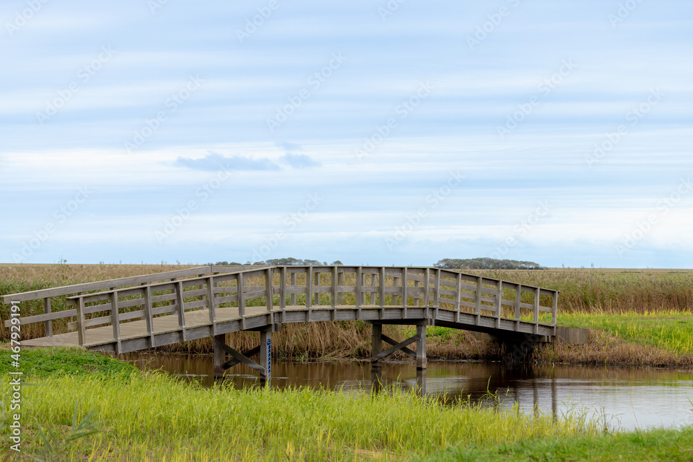 Countryside landscape with flat and low land under blue sky and white clouds, Typical Dutch polder land with wooden bridge crossing the canal or small ditch, Texel Island, Noord Holland, Netherlands.