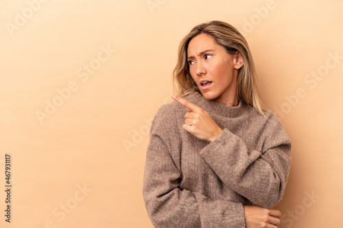 Young caucasian woman isolated on beige background points with thumb finger away, laughing and carefree.