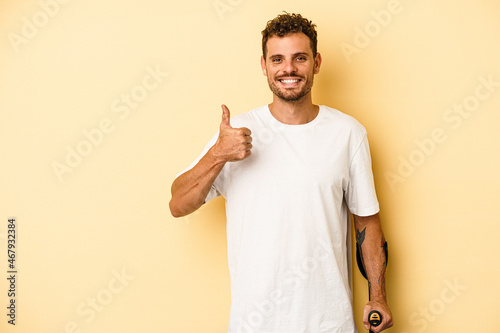 Young caucasian man holding crutch isolated on yellow background smiling and raising thumb up photo