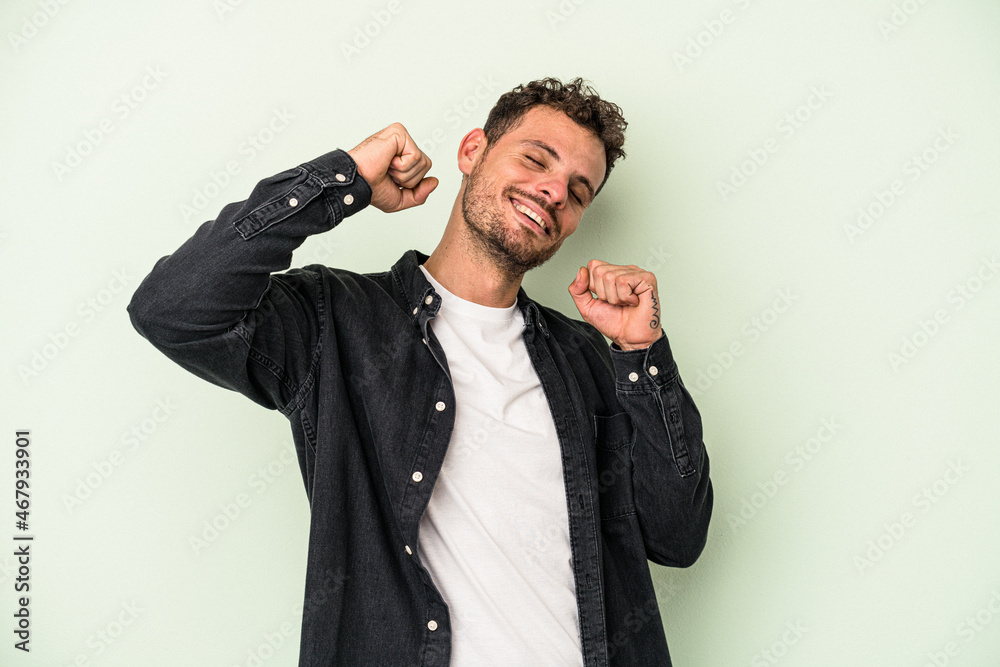 Young caucasian man isolated on green background celebrating a special day, jumps and raise arms with energy.