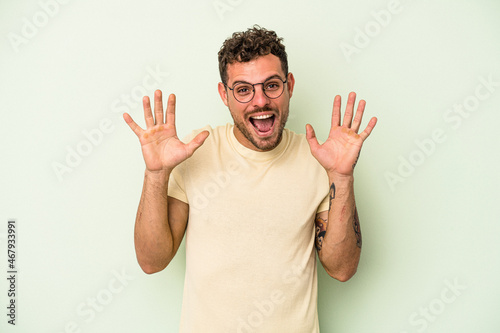 Young caucasian man isolated on green background receiving a pleasant surprise, excited and raising hands.