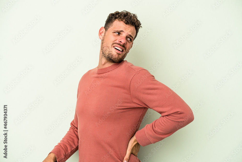 Young caucasian man isolated on green background suffering a back pain. Young caucasian man isolated on green background suffering a back pain.