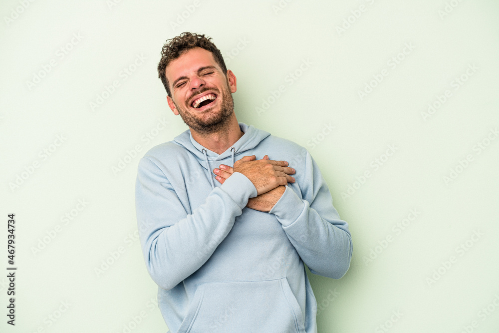 Young caucasian man isolated on green background laughing keeping hands on heart, concept of happiness. Young caucasian man isolated on green background laughing keeping hands on heart, concept of happiness.