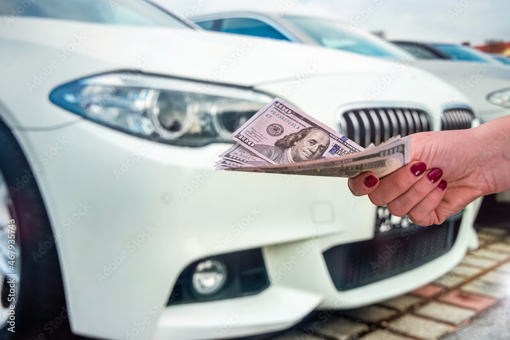 well-groomed female hands holding beautiful new dollar banknotes near cars well-groomed female hands holding beautiful new dollar banknotes near cars
