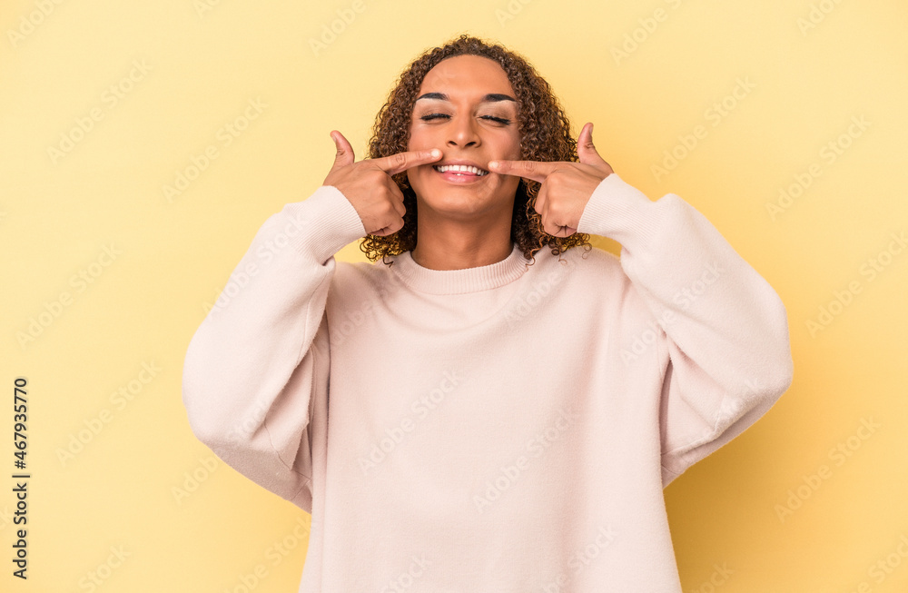 Young latin transsexual woman isolated on yellow background smiles, pointing fingers at mouth. Young latin transsexual woman isolated on yellow background smiles, pointing fingers at mouth.