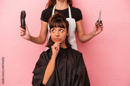 Young mixed race woman getting a haircut at the hairdresser isolated on pink background looking sideways with doubtful and skeptical expression.