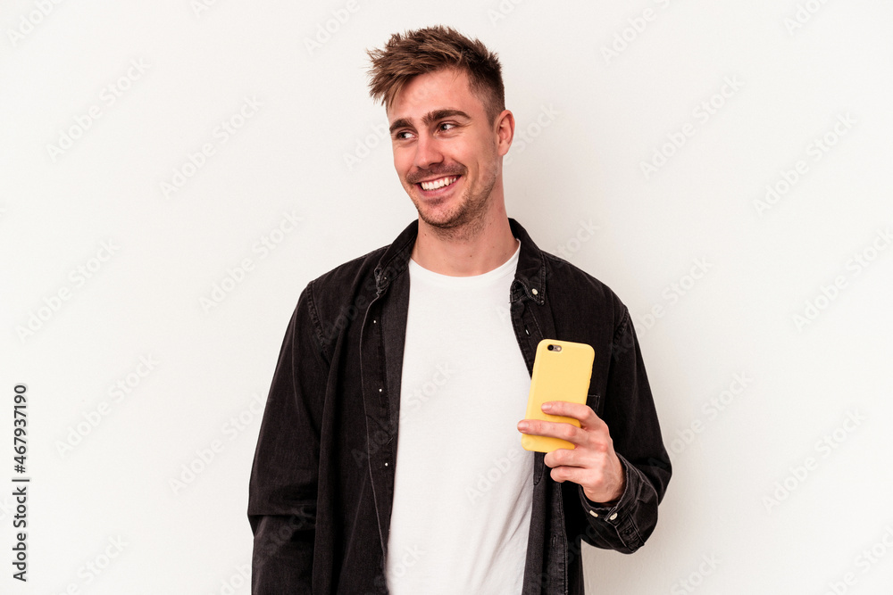 Young caucasian man holding a mobile phone isolated on white background looks aside smiling, cheerful and pleasant. Young caucasian man holding a mobile phone isolated on white background looks aside smiling, cheerful and pleasant.