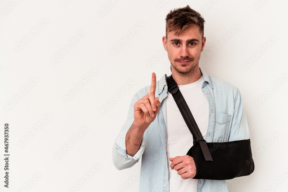 Young caucasian man with broken hand isolated on white background showing number one with finger. Young caucasian man with broken hand isolated on white background showing number one with finger.
