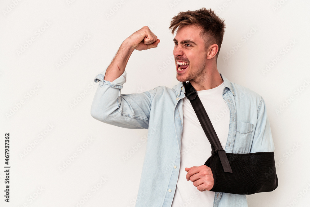 Young caucasian man with broken hand isolated on white background raising fist after a victory, winner concept. Young caucasian man with broken hand isolated on white background raising fist after a victory, winner concept.