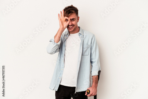 Young caucasian man holding crutch isolated on white background excited keeping ok gesture on eye. photo