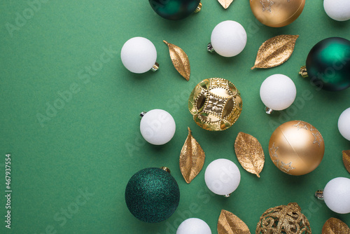 Top view photo of gold white and green christmas tree balls and golden leaves on isolated green background with empty space
